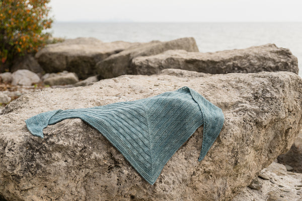 handknit triangle scarf laying on rocks
