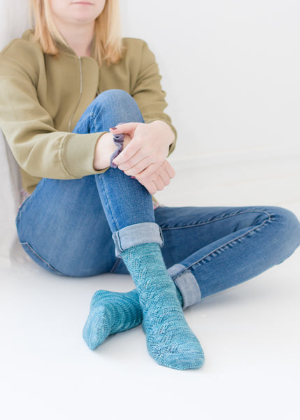 Woman sitting up against a wall modelling hand knit socks